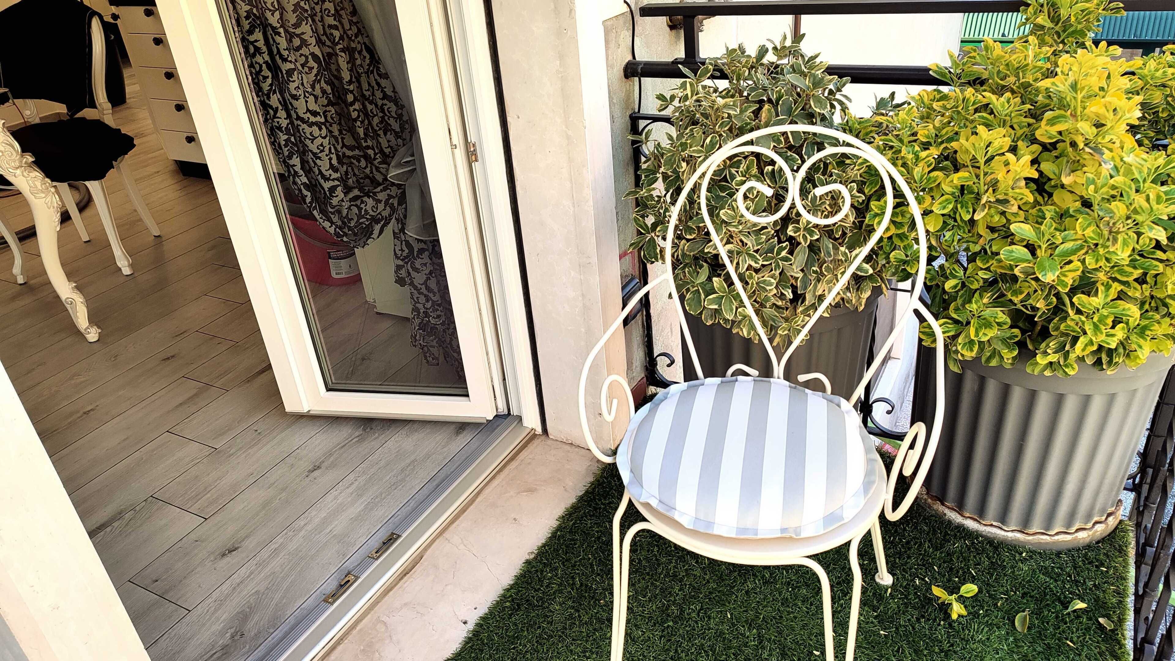 A chair with a heart-shaped backrest and a striped cushion, positioned on a balcony with artificial grass and potted plants.