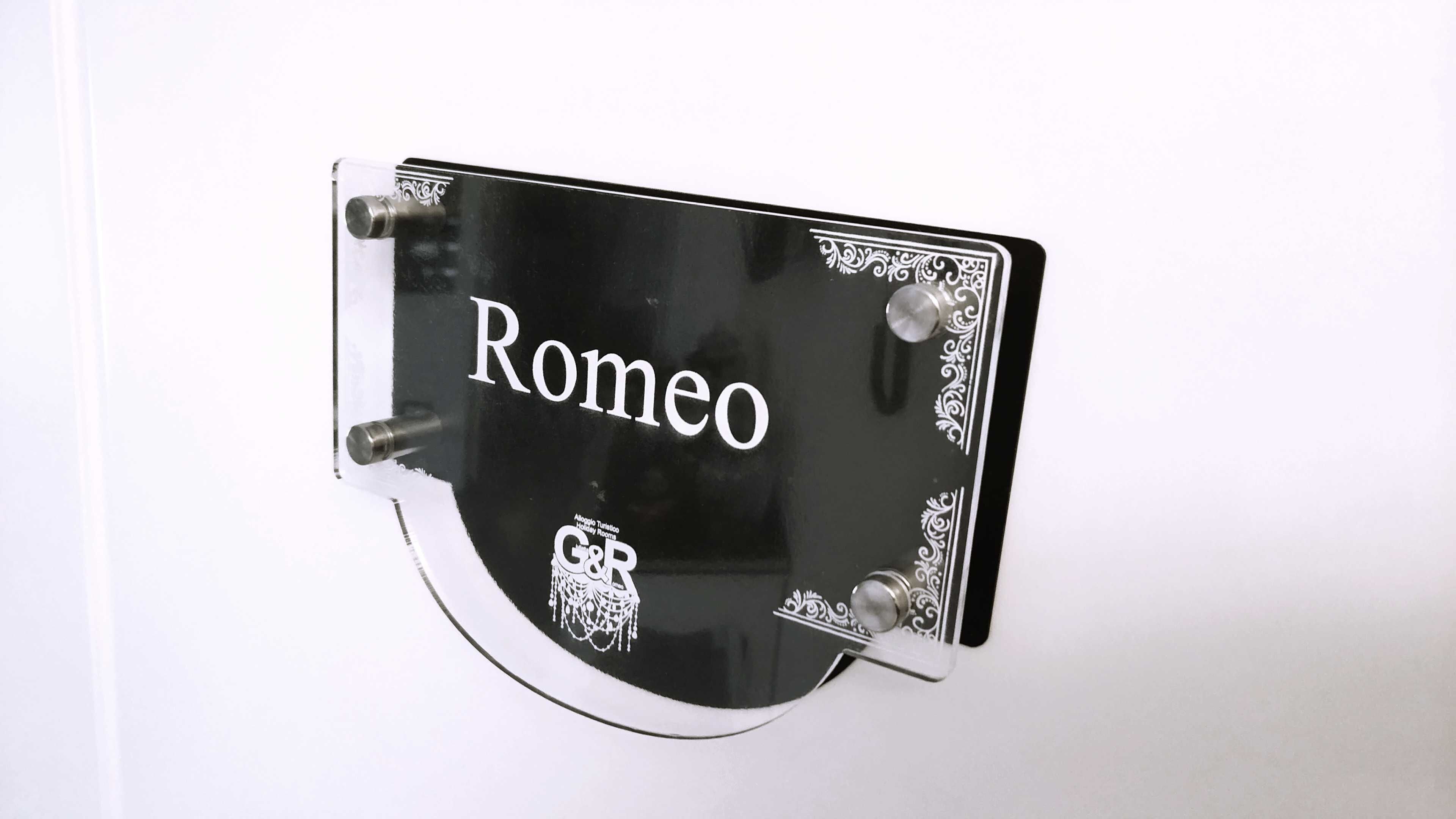 A black sign with the word 'Romeo' and a small owl illustration, mounted on a white wall.
