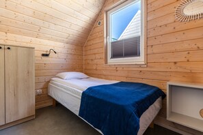 A single bed with a blue blanket, a wooden wardrobe, a bedside table, and a window with blinds. - Comfortable holiday homes with SPA Rewal (Rewal)