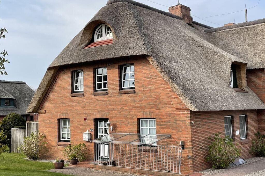 Une maison en briques avec un toit de chaume et une véranda en verre.