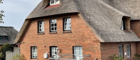 A brick house with a thatched roof and a glass conservatory.