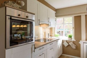Una cocina con armarios blancos, horno empotrado, ventana con vistas y un lavabo.