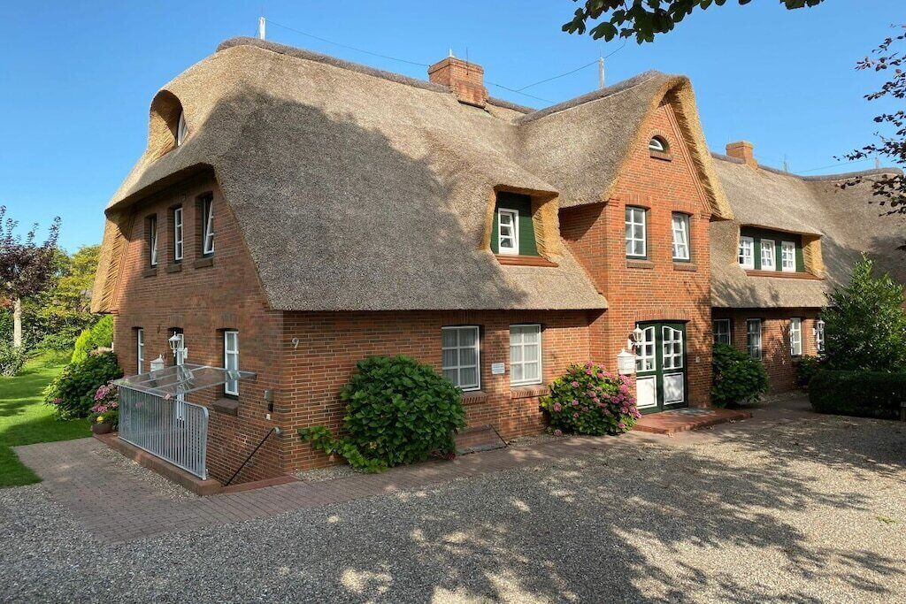 A two-story brick house with a thatched roof, a small front porch, and a gravel driveway.