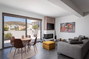 A modern living room with a dining area, a fireplace, and a large window offering a view of the city. - Aelia Riviera Apartment (Vari)