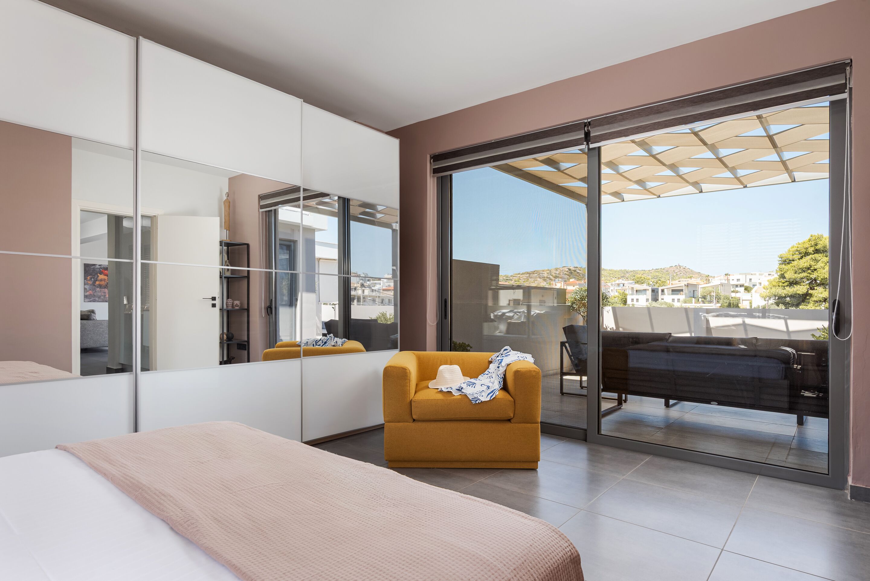 A modern bedroom with a large bed, a sofa, a wardrobe, and a sliding glass door leading to a balcony.