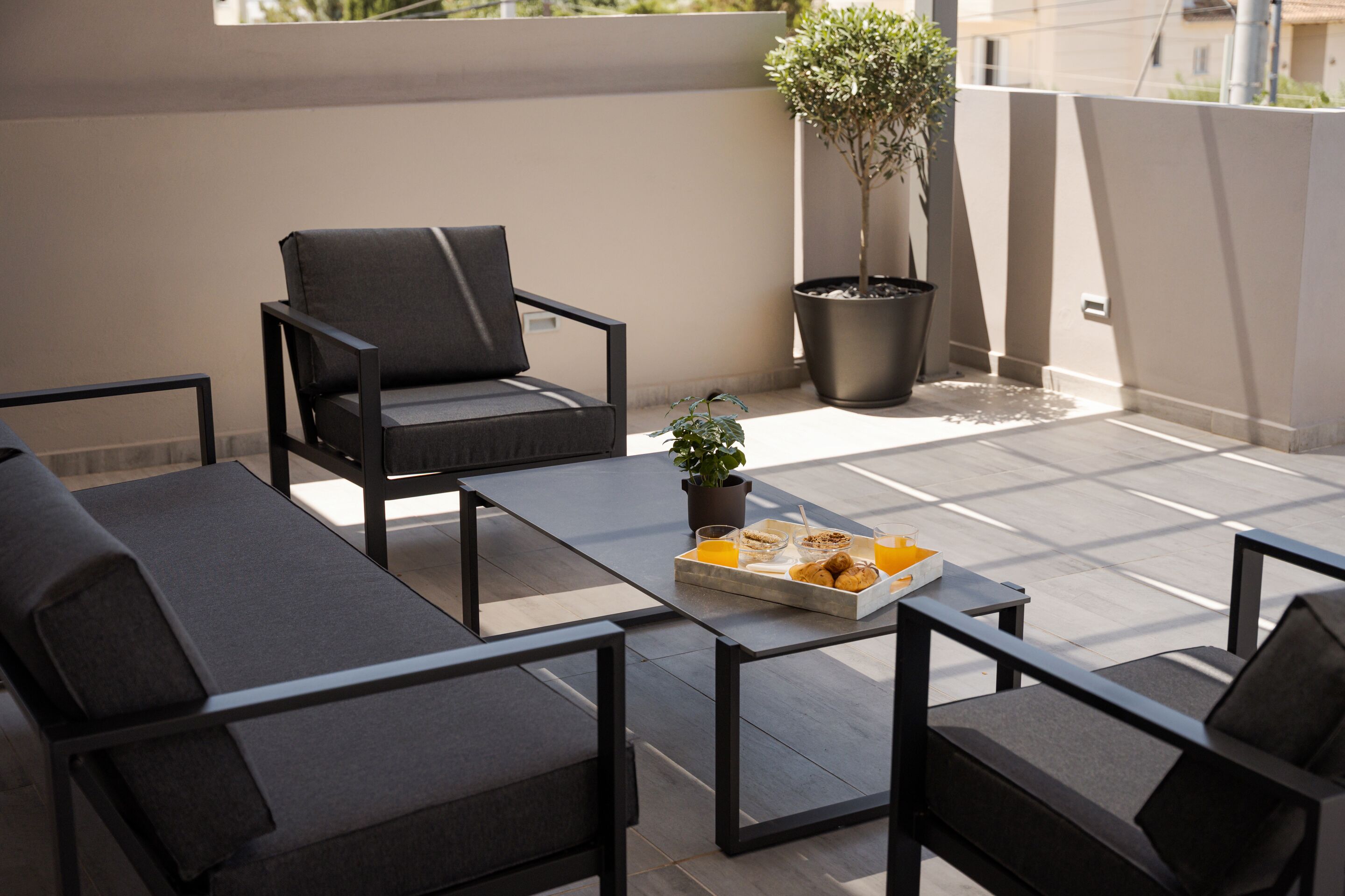 A modern outdoor seating area with a sofa, chairs, and a table. There is a tray with food and drinks on the table.