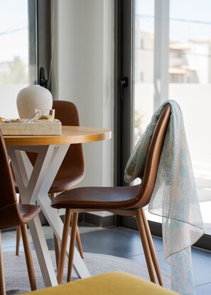 A dining area with a round table, chairs, and a view through a glass door. - Aelia Riviera Apartment (Vari)