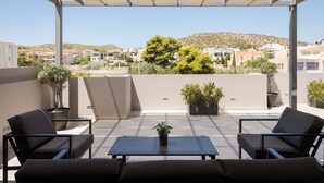 Una terraza en la azotea con una pérgola, dos sillas, una mesa y plantas en macetas.