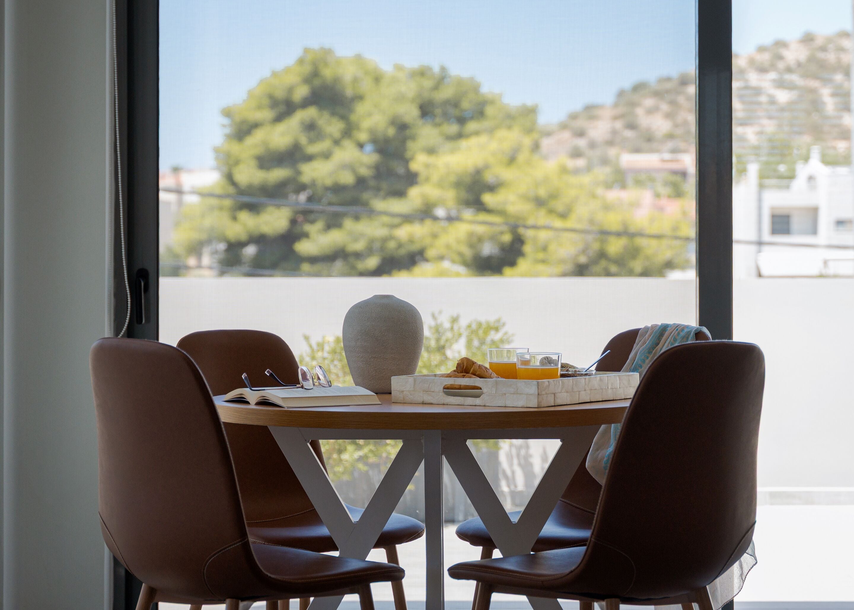 A dining area with a table set for two, a book, glasses, a croissant, and a tray with orange juice.