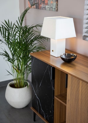 A modern interior with a wooden cabinet, a white lamp, a potted plant, and a marble-patterned cabinet door. - Aelia Riviera Apartment (Vari)