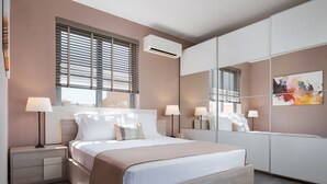Un dormitorio moderno con cama, lámparas de noche, mesita de noche, un espejo grande y una ventana con persianas.
