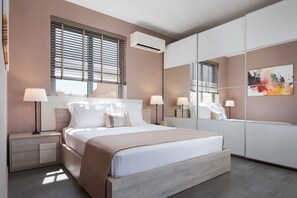Ein modernes Schlafzimmer mit einem Bett, Nachttischlampen, einem Nachttisch, einem großen Spiegel und einem Fenster mit Jalousien.