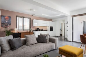A modern living room with a grey patterned sofa, a mustard-colored ottoman, and a coffee table. - Aelia Riviera Apartment (Vari)