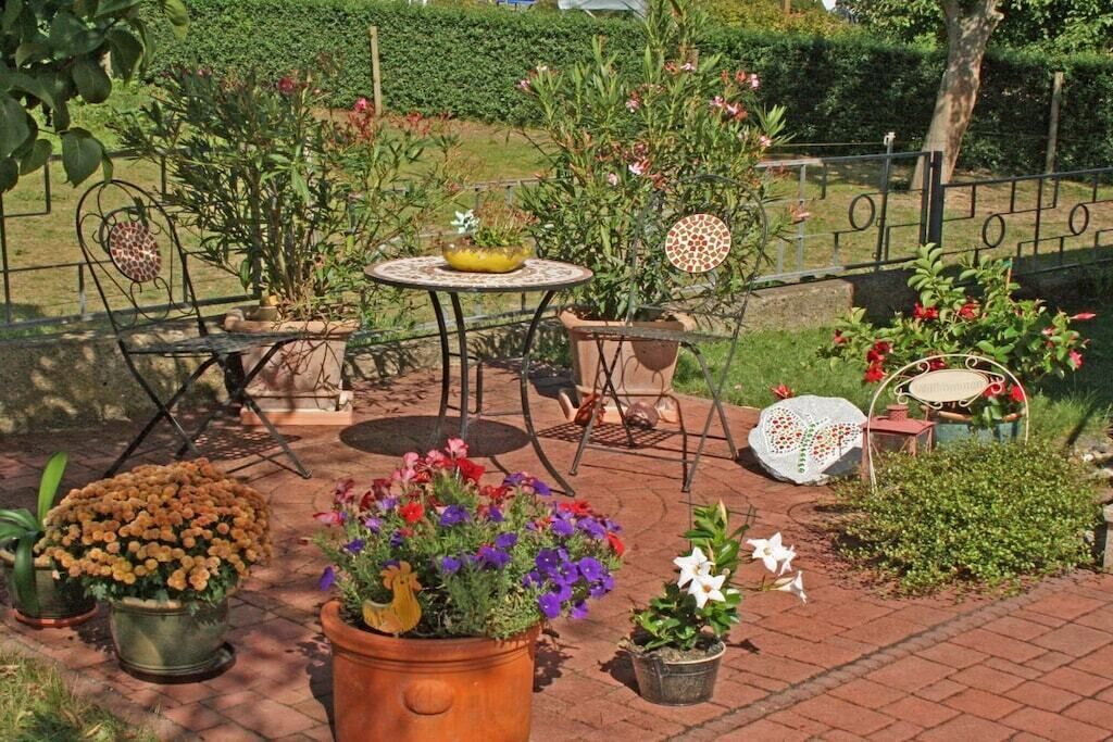 An outdoor patio area with a table and chairs, surrounded by potted plants and flowers.