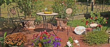 An outdoor patio area with a table and chairs, surrounded by potted plants and flowers.