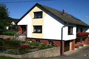 Ein zweistöckiges Haus mit Satteldach, einer Satellitenschüssel und einem kleinen Garten mit Blumen.