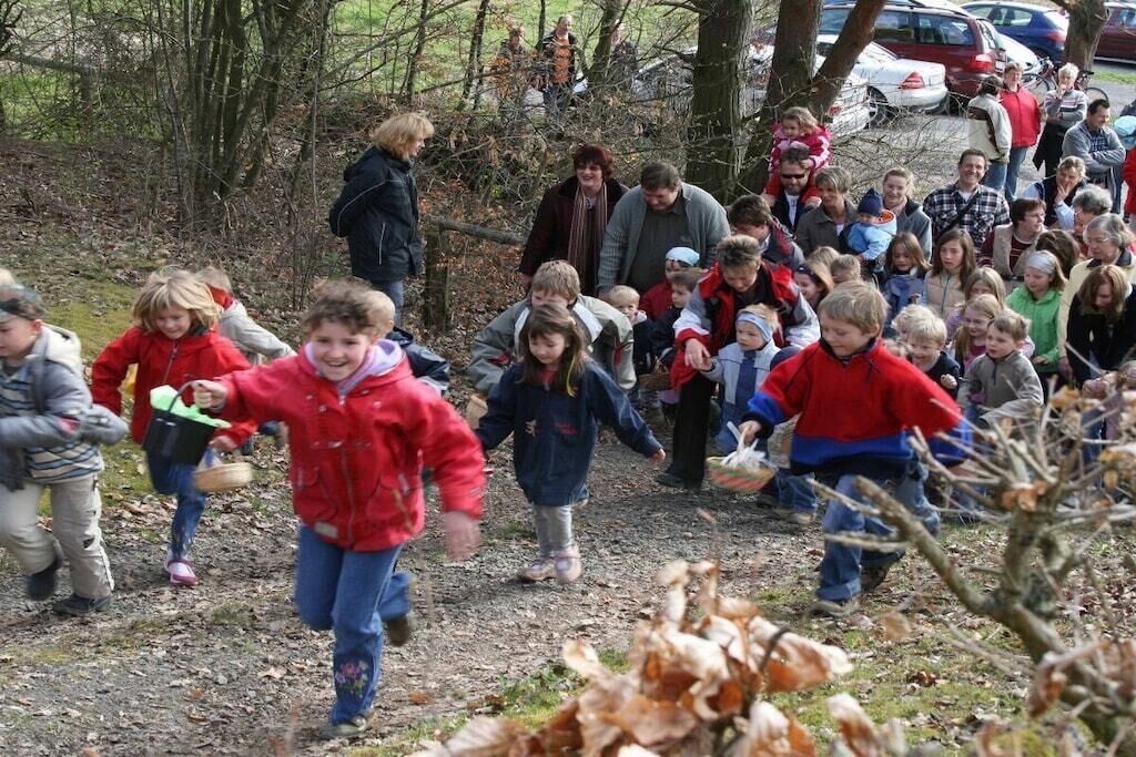 Um grupo de crianças e adultos em ambiente externo, com árvores e uma trilha de terra.
