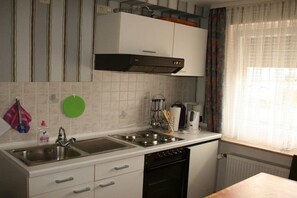 Eine Küche mit Spüle, Herd und Backofen, sowie einem Fenster und Vorhängen.