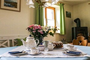 Une table à manger dressée avec un service à thé et un gâteau, un vase rempli de fleurs et une cheminée en arrière-plan.