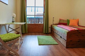 Une petite pièce agréable et chaleureuse, avec un lit en bois, un fauteuil vert, une petite table et une fenêtre avec des rideaux.
