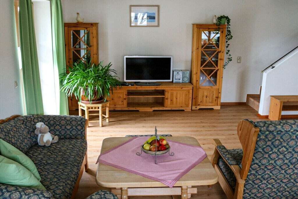 Ein Wohnzimmer mit Fernseher, Holzmöbeln, einer Topfpflanze und einer Obstschale auf einem Tisch.