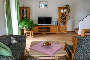 Un salon avec un téléviseur, des meubles en bois, une plante en pot et un panier de fruits posé sur une table.