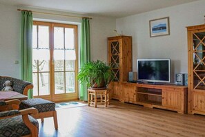 Un salon avec un canapé, un téléviseur, un meuble en bois et une plante en pot.