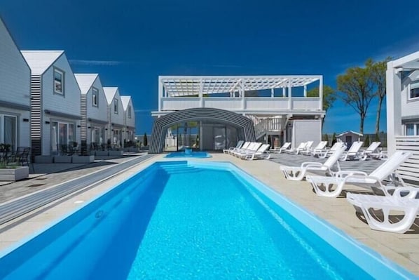 A swimming pool with lounge chairs, a covered area, and modern buildings. - Comfortable holiday homes with SPA Rewal (Rewal)