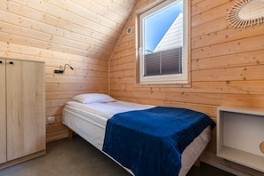 A single bed with a blue blanket, a wooden wardrobe, a bedside table, and a window with blinds. - Comfortable holiday homes with SPA Rewal (Rewal)