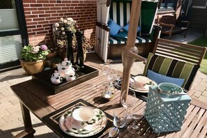 Un patio al aire libre con una mesa dispuesta para una comida, rodeado de sillas y un sofá de mimbre.