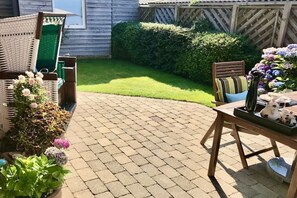 Un patio con piso de ladrillo, mobiliario de mimbre y una mesa con adornos.