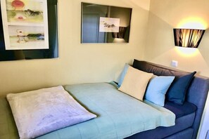 Ein Zimmer mit einem Bett, einem Schlafsofa, einer Wandleuchte und einem gerahmten Kunstwerk.