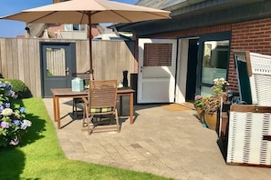 A patio with a table and chairs, a wooden fence, and a door leading to a garage. - Holiday apartment with 1 bedroom (Sylt OT Westerland)