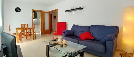 A living room with a blue sofa, a glass coffee table, a red chair, and a television.