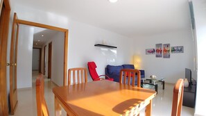 A modern living room with a wooden dining table, red chairs, a blue sofa, and a coffee table.
