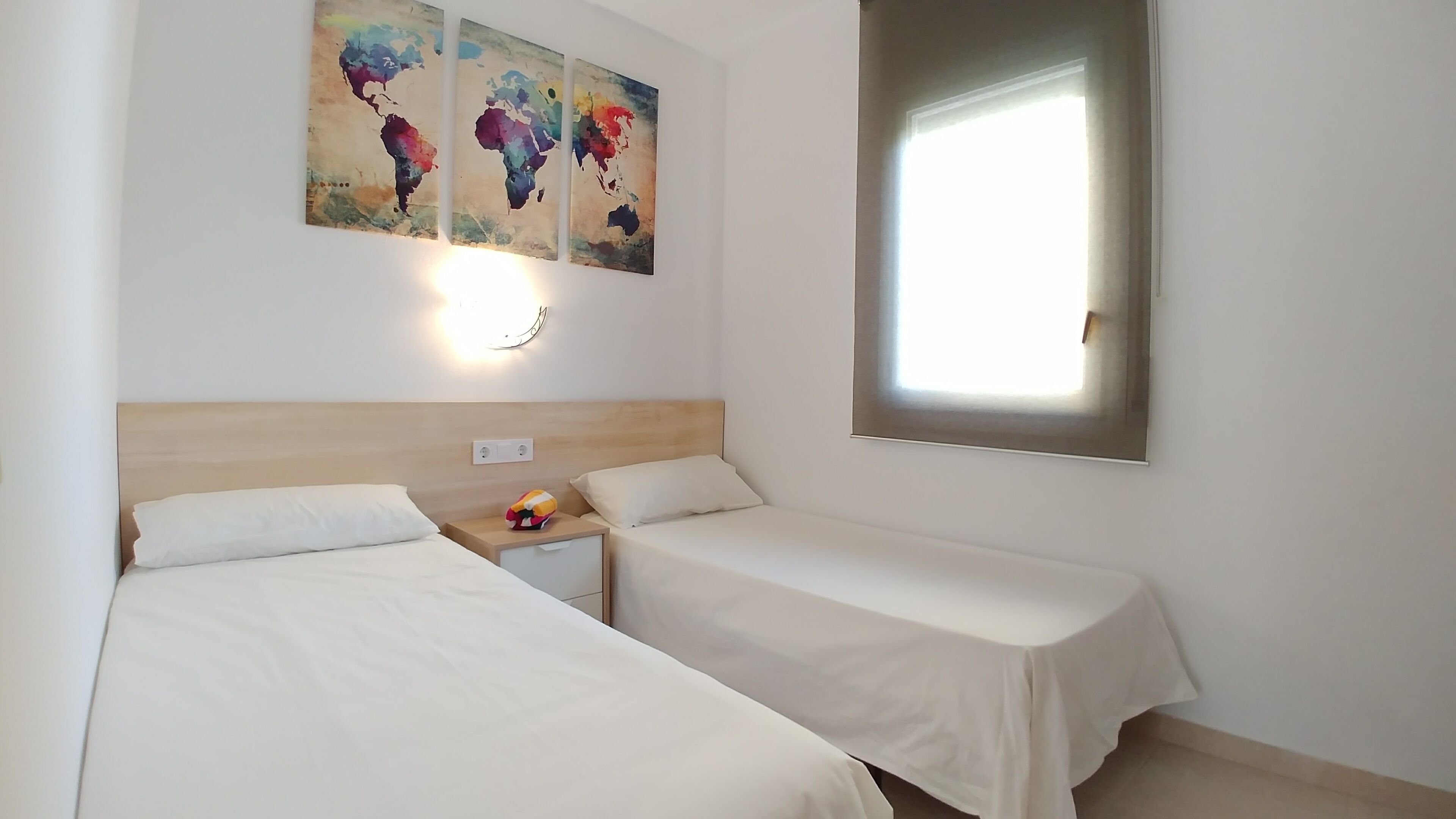 Ein Hotelzimmer mit zwei Einzelbetten, einem Nachttisch mit Lampe und einem großen Fenster.
