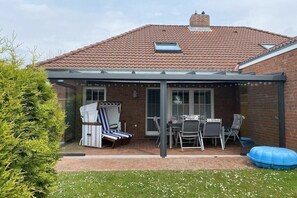 Eine überdachte Terrasse mit Gartenmöbeln, ein Ziegelhaus und ein klarer Himmel.