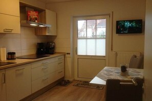Eine kompakte Küche mit Fenster, einer Kaffeemaschine und einem an der Wand befestigten Fernseher.