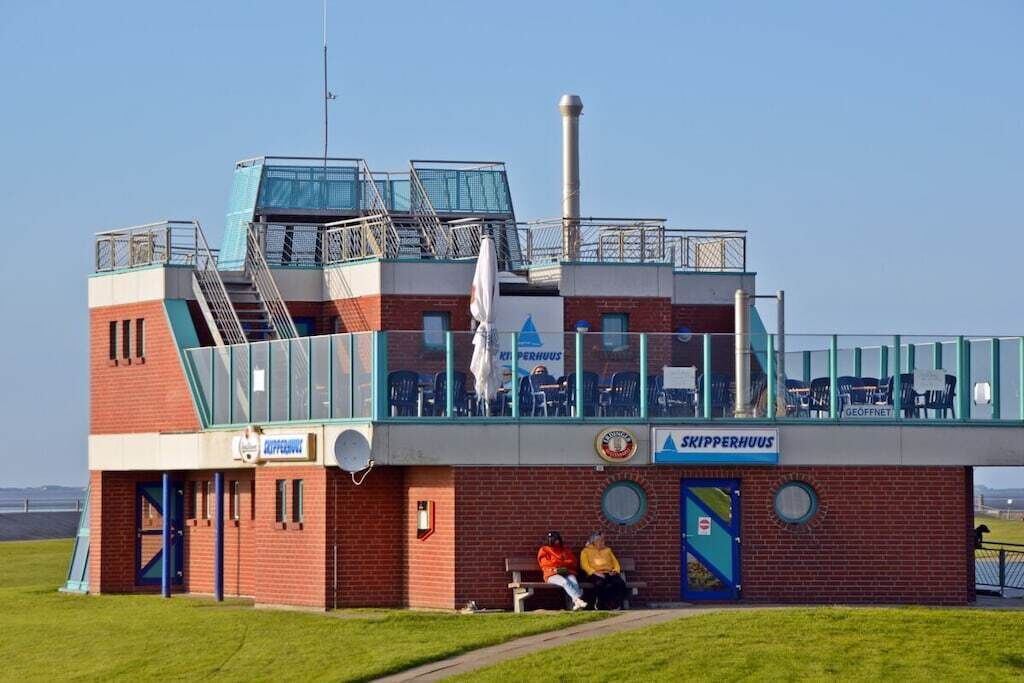 A building with a brick facade, a glass enclosure with chairs, and a sign reading 'SKIPPERHUUS'.