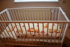 Ein weißes Babybett mit einer Matratze, verziert mit Zeichentrickfiguren, und einem Fenster darüber.