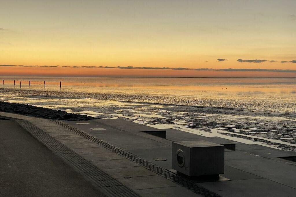 A coastal walkway with a concrete barrier and a drainage grate.