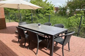 Eine Terrasse mit Tisch und Stühlen, umgeben von einem Pflasterboden und einem Zaun.