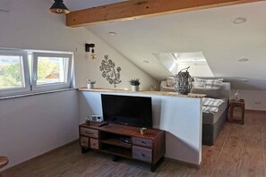Ein Schlafzimmer im Loft-Stil mit schrägem Dach, einem Bett, einem Fernseher, einem kleinen Schreibtisch und einem Fenster.
