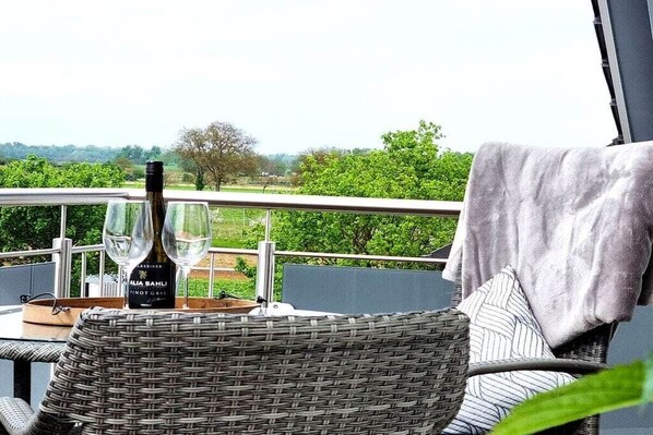 Een balkon met rieten meubels, een fles wijn en glazen.