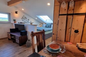 Ein gemütliches Zimmer mit Schlafkoje, einem Esstisch mit Schüssel und Weinglas, einem Fernseher und einem Schreibtisch mit Computer.