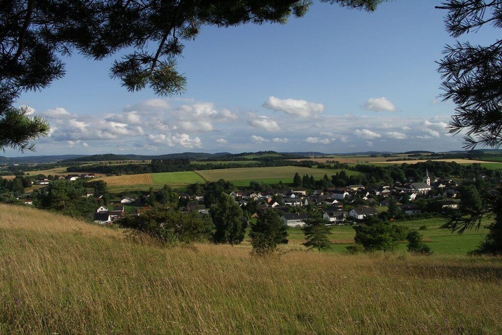 A rural landscape with a village, rolling hills, and a clear sky.