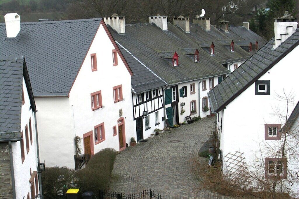 A cobblestone street with traditional buildings, including a white house with a red door and a black and white timber-framed structure.