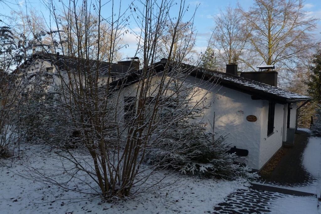 Une maison recouverte de neige, avec un petit porche et un chemin menant à l’entrée.