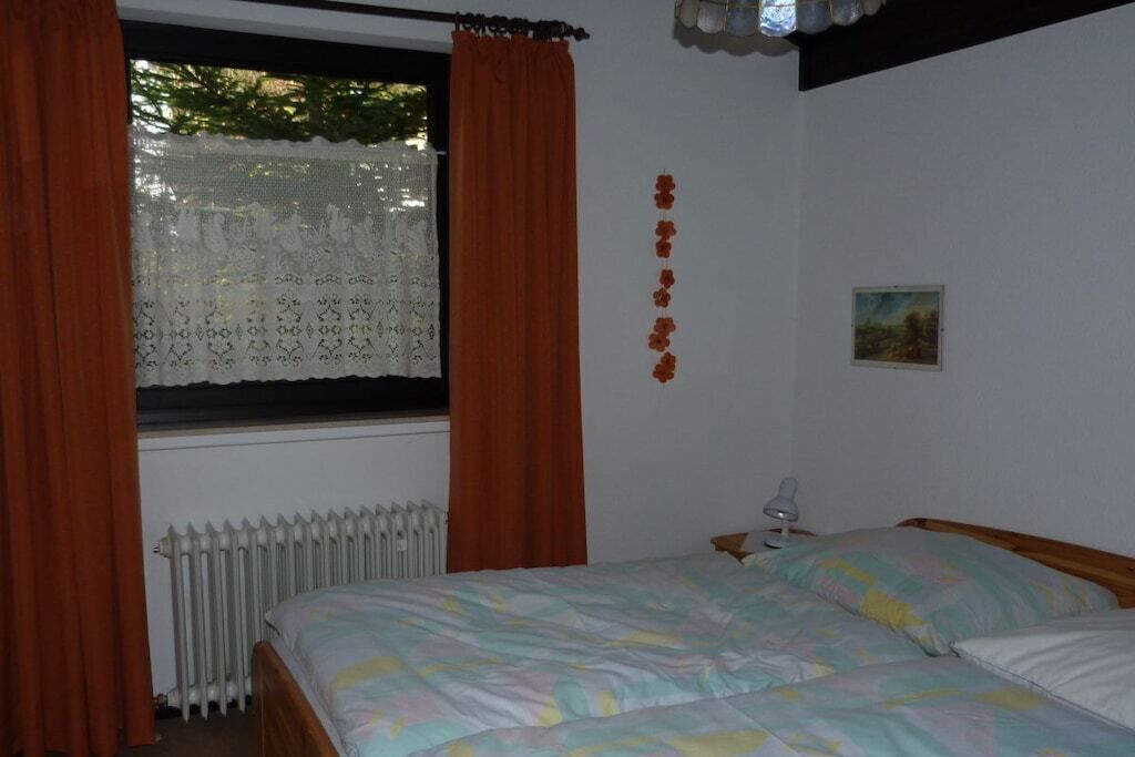Een slaapkamer met een bed, een raam met gordijnen, een radiator en een klein nachtkastje met een lamp.