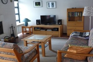 Ein Wohnzimmer mit Fernseher, Lautsprechern, Bücherregal und einer Couch.